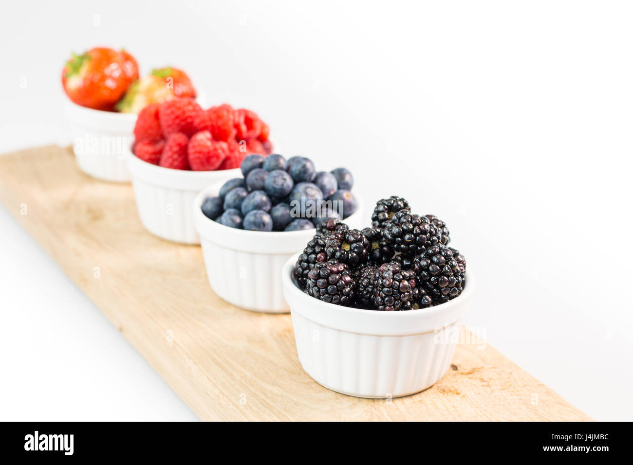 Blackberries, blueberries, raspberries and strawberries on wooden cutting board with shallow depth of field Stock Photo