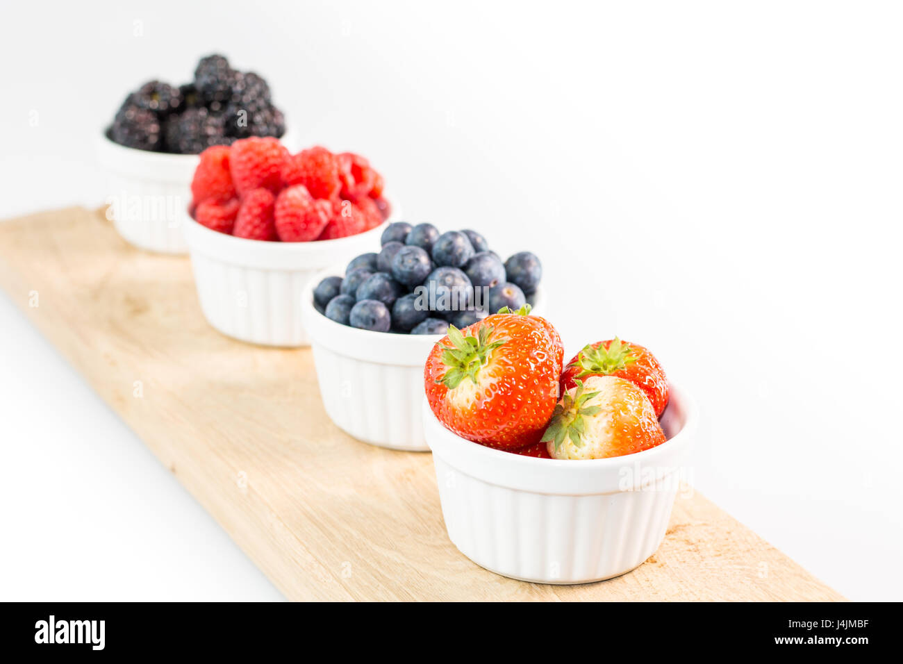 Strawberries, blueberries, raspberries and blackberries on wooden cutting board with shallow depth of field Stock Photo