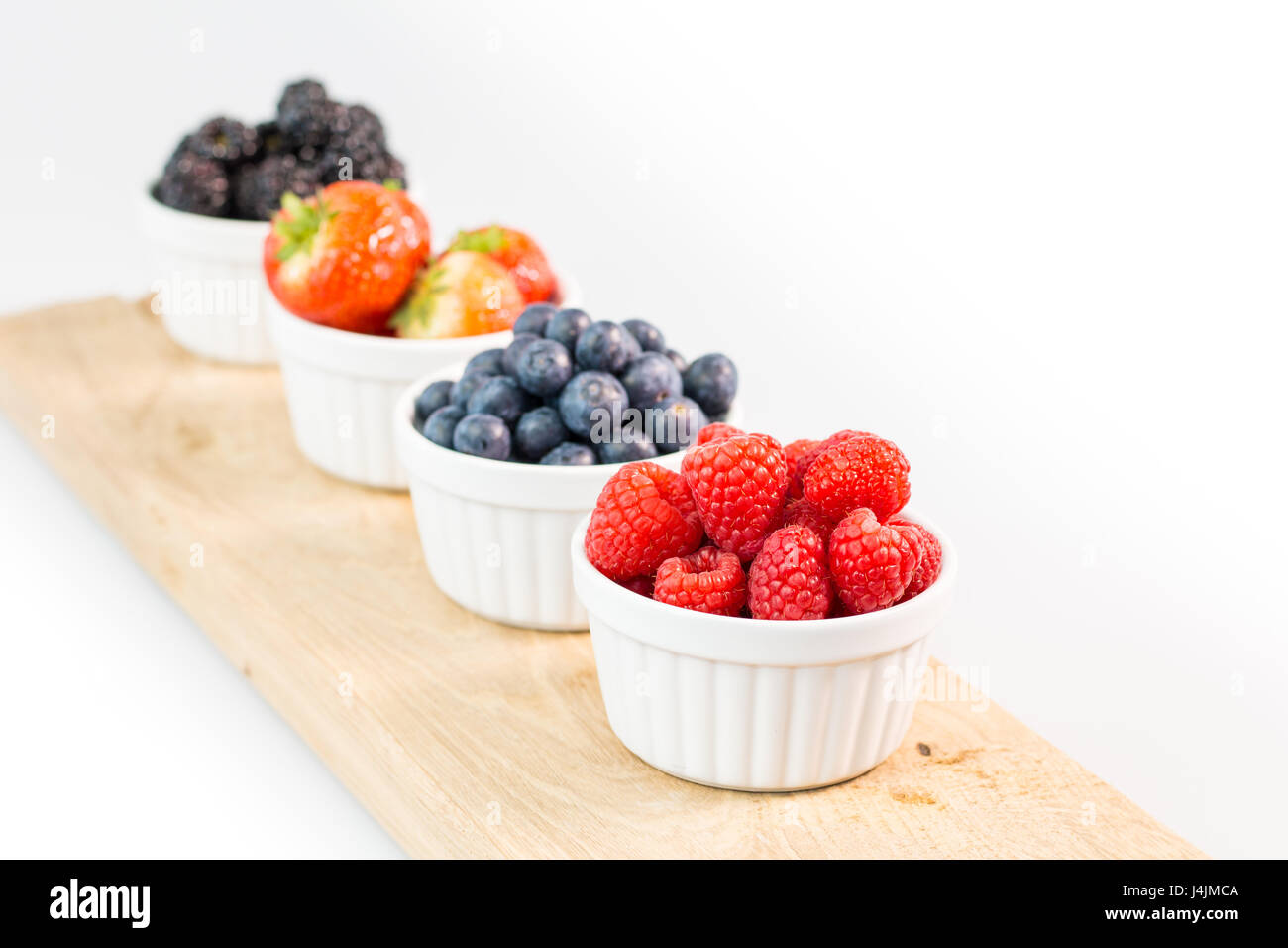 Raspberries, blueberries, strawberries and blackberries on wooden cutting board with shallow depth of field Stock Photo