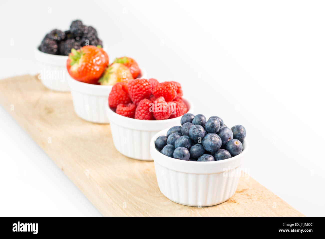Blueberries, raspberries, strawberries and blackberries on wooden cutting board with shallow depth of field Stock Photo