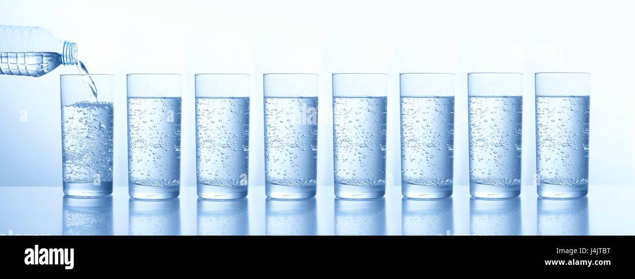 Pouring water from a bottle into multiple glasses, studio shot Stock Photo