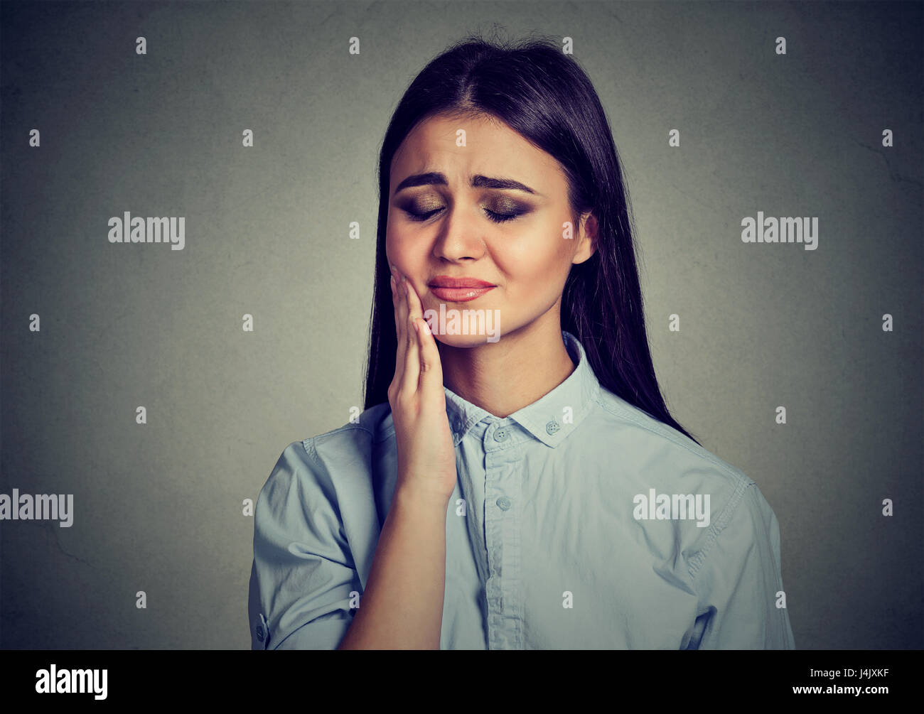 Woman with sensitive toothache crown problem suffering from pain touching outside mouth with hand isolated on gray background. Negative human emotion  Stock Photo