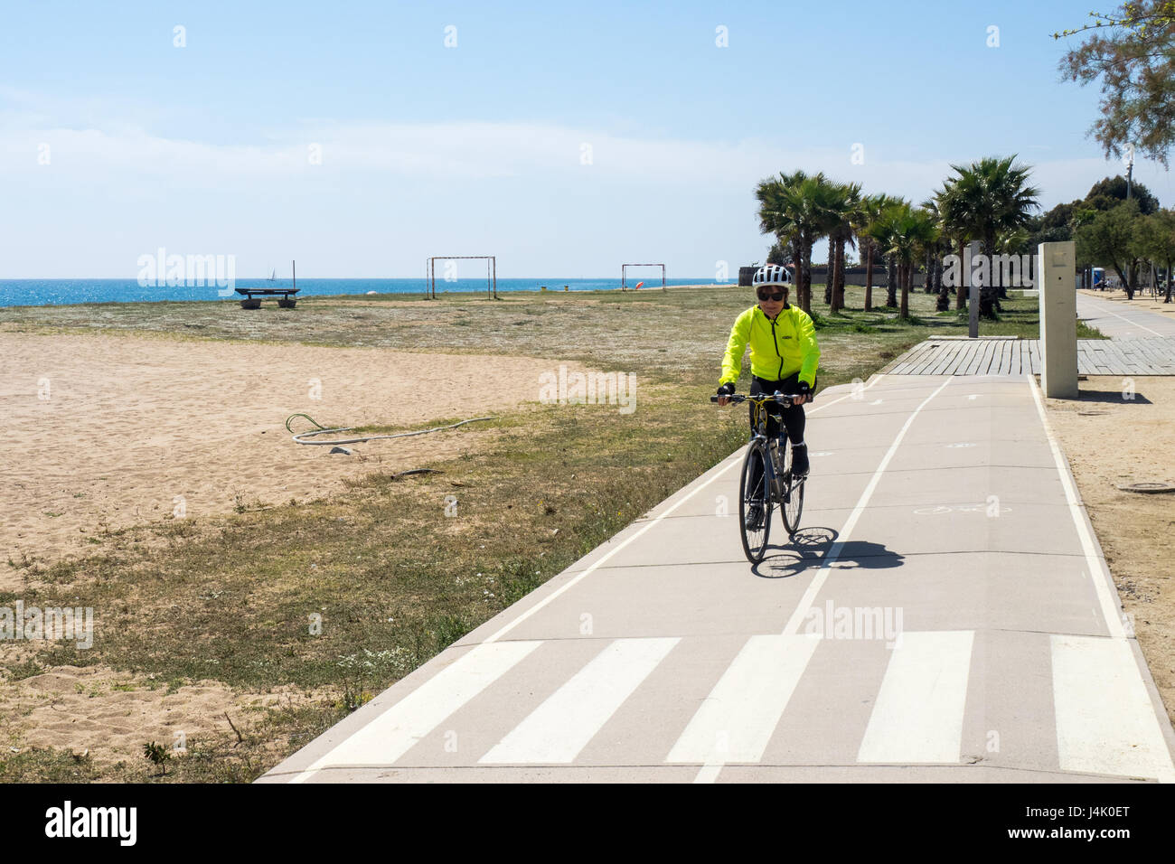 A female touring cyclist riding on a bike path  on the beachfront approaching Malgrat de Mar, Catalonia, Spain. Stock Photo