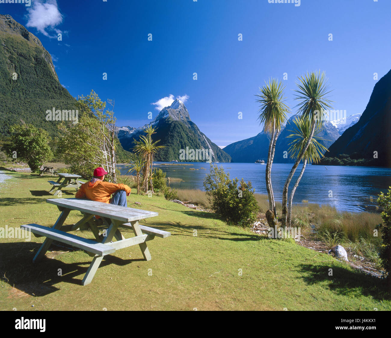 New Zealand, south island, fjord country national park, Mitre Peak, shore, wooden bank, tourist, back view New Zealand, mountain landscape, mountain, mountains, coast, fjord, lakeside, park-bench, man, détente, rest, view, enjoy, take it easy, destination, place of interest, nature rest, silence, Idyll Stock Photo