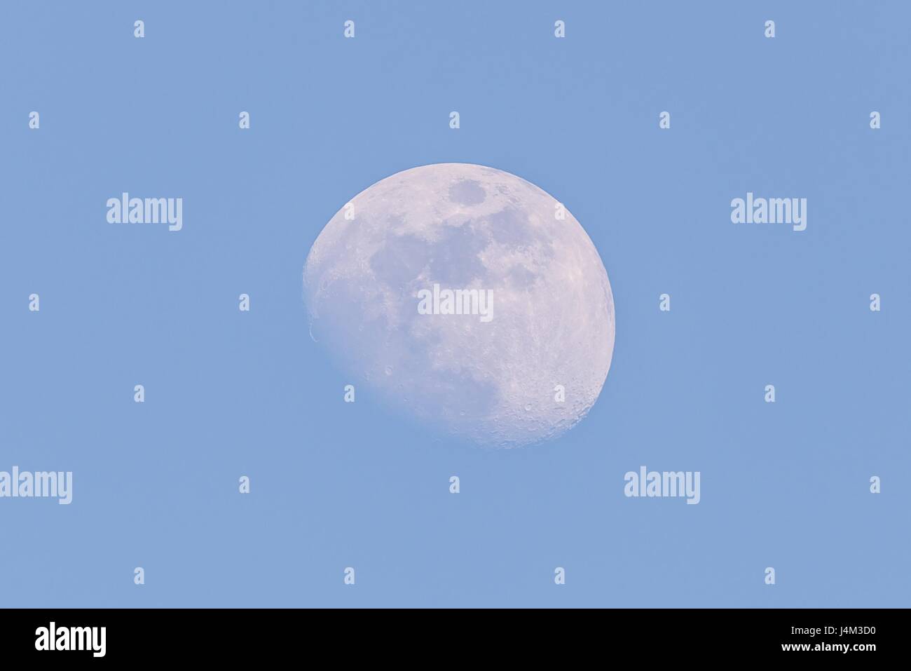 Horizontal photo of white big moon. Moon is captured during a day time with clear blue sky and few days before full-moon so only small part is hidden  Stock Photo