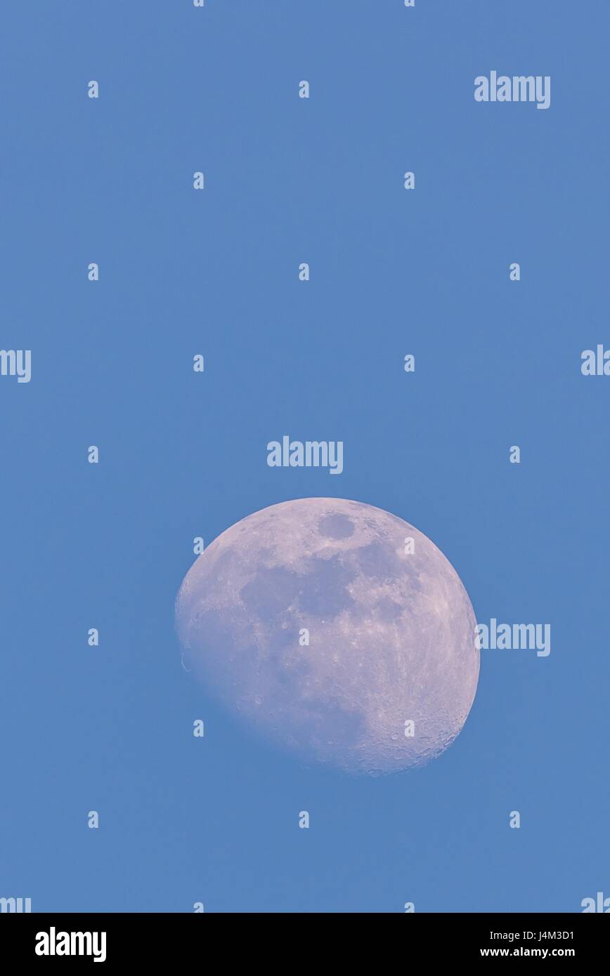 Vertical photo of white big moon. Moon is captured during a day time with clear blue sky and few days before full-moon so only small part is hidden in Stock Photo
