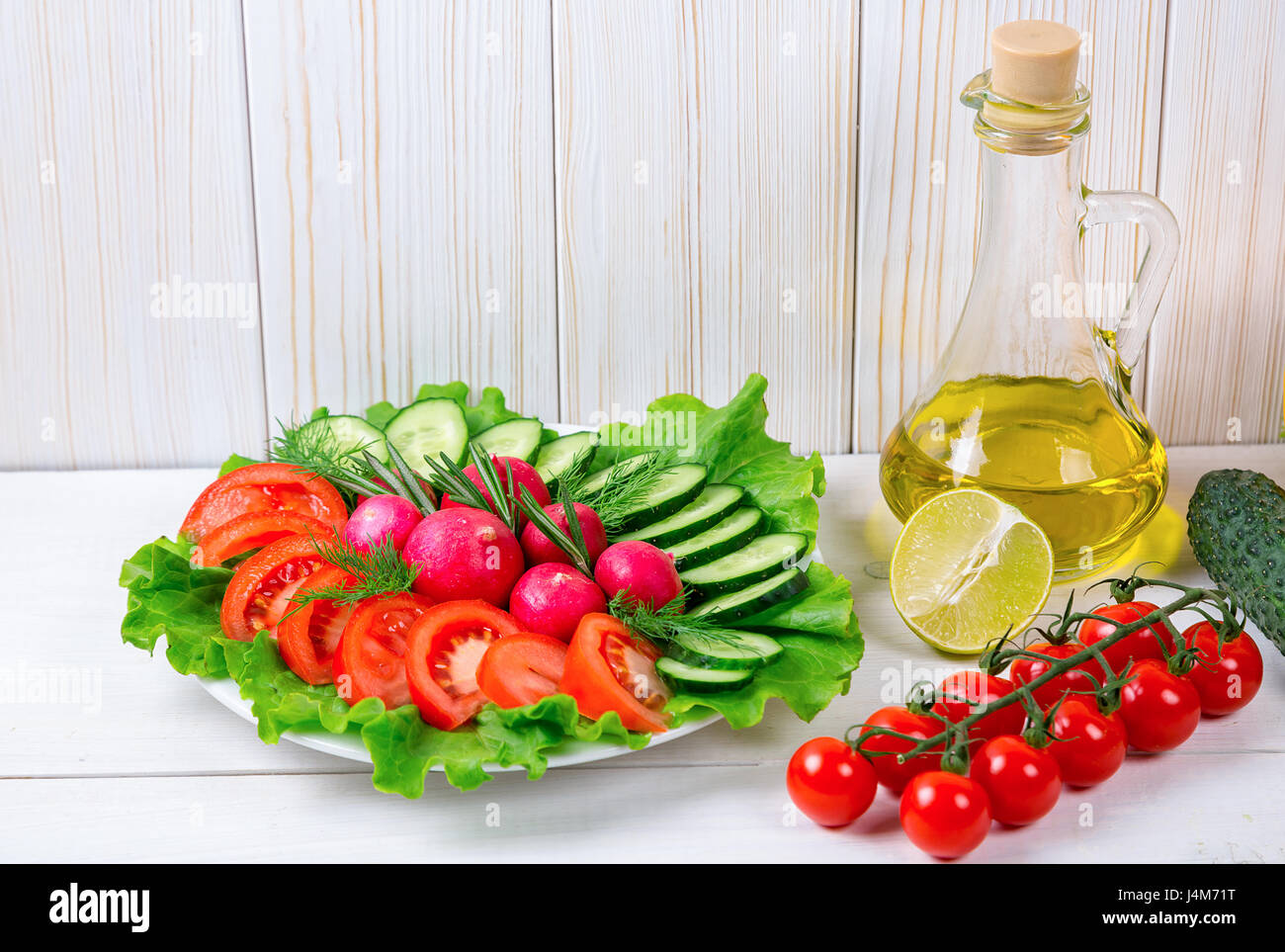 Cucumbers, radish, tomatoes cherry, olive oil, herb and spices on old white wooden background. Set for healthy foods. Ingredients for salad. Stock Photo