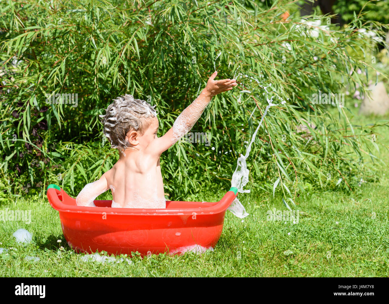 Preschooler boy taking bath outdoors playing with suds foam in washing basin Stock Photo
