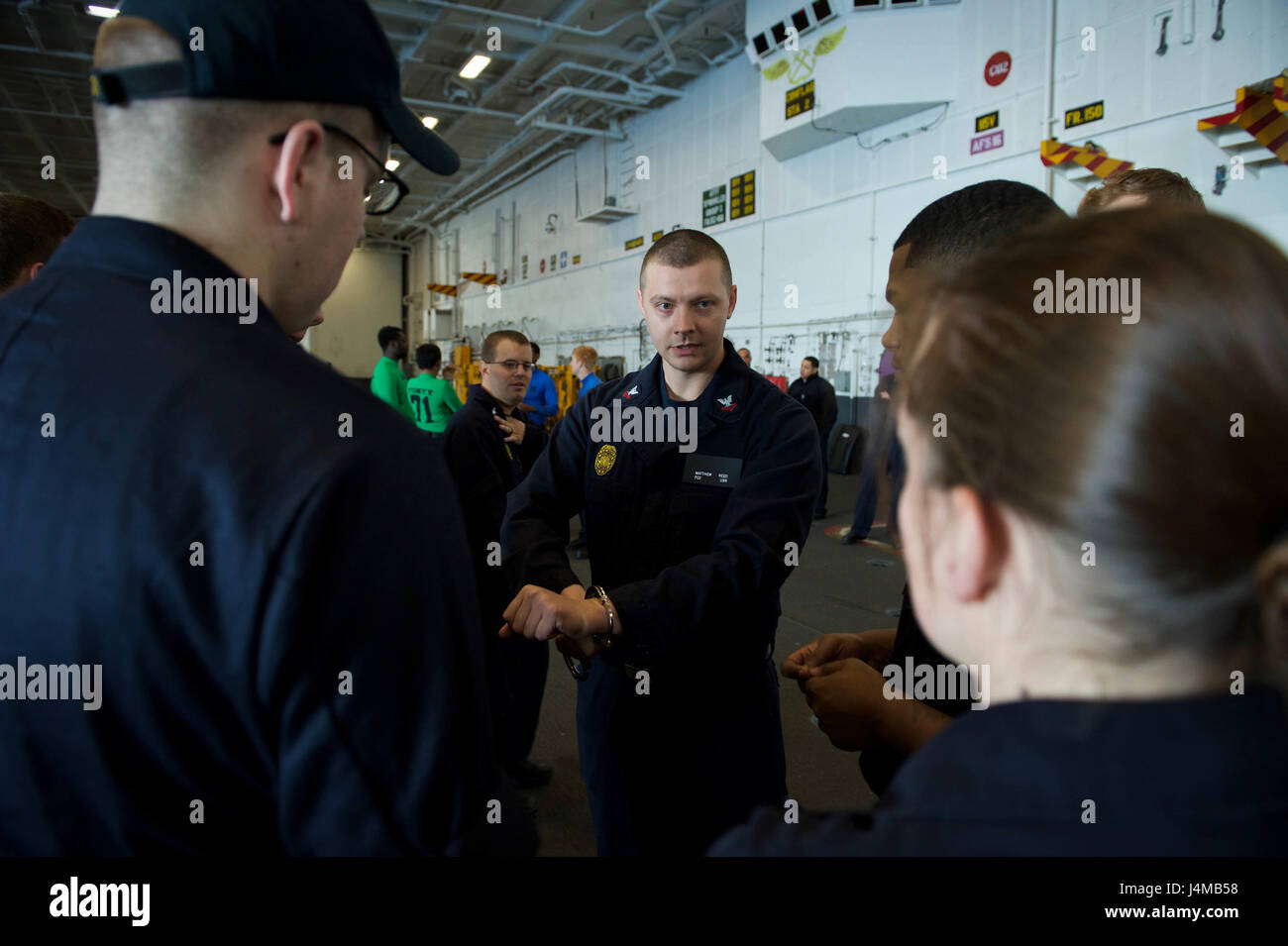 170117-N-SK327-012 PACIFIC OCEAN (Jan. 17, 2017) Master-at-arms 2nd class Matthew Reed instructs Sailors in the proper use of handcuffs during Security Reaction Force-Basic training in the hangar bar of the aircraft carrier USS Theodore Roosevelt (CVN 71). Theodore Roosevelt is currently conducting basic training off the coast of Southern California. (U.S. Navy photo by Mass Communication Seaman Rachael Treon/Released) Stock Photo