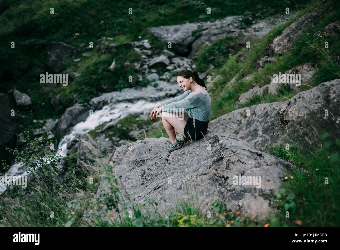 Smiling Caucasian woman sitting on rock on hill Stock Photo