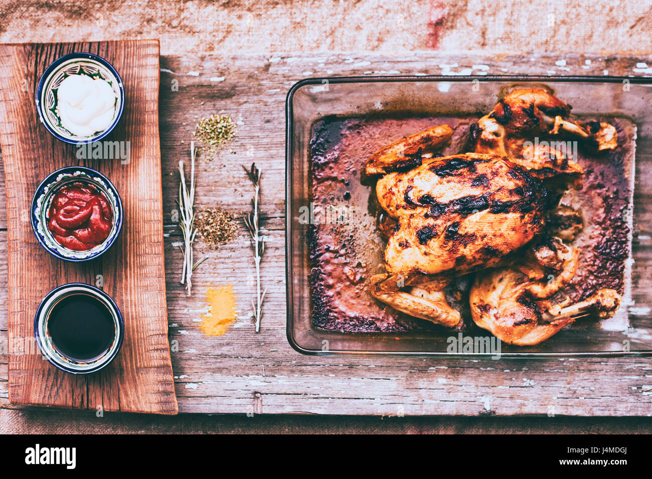 Close up of roasted chicken with rosemary and sauces on wooden table Stock Photo