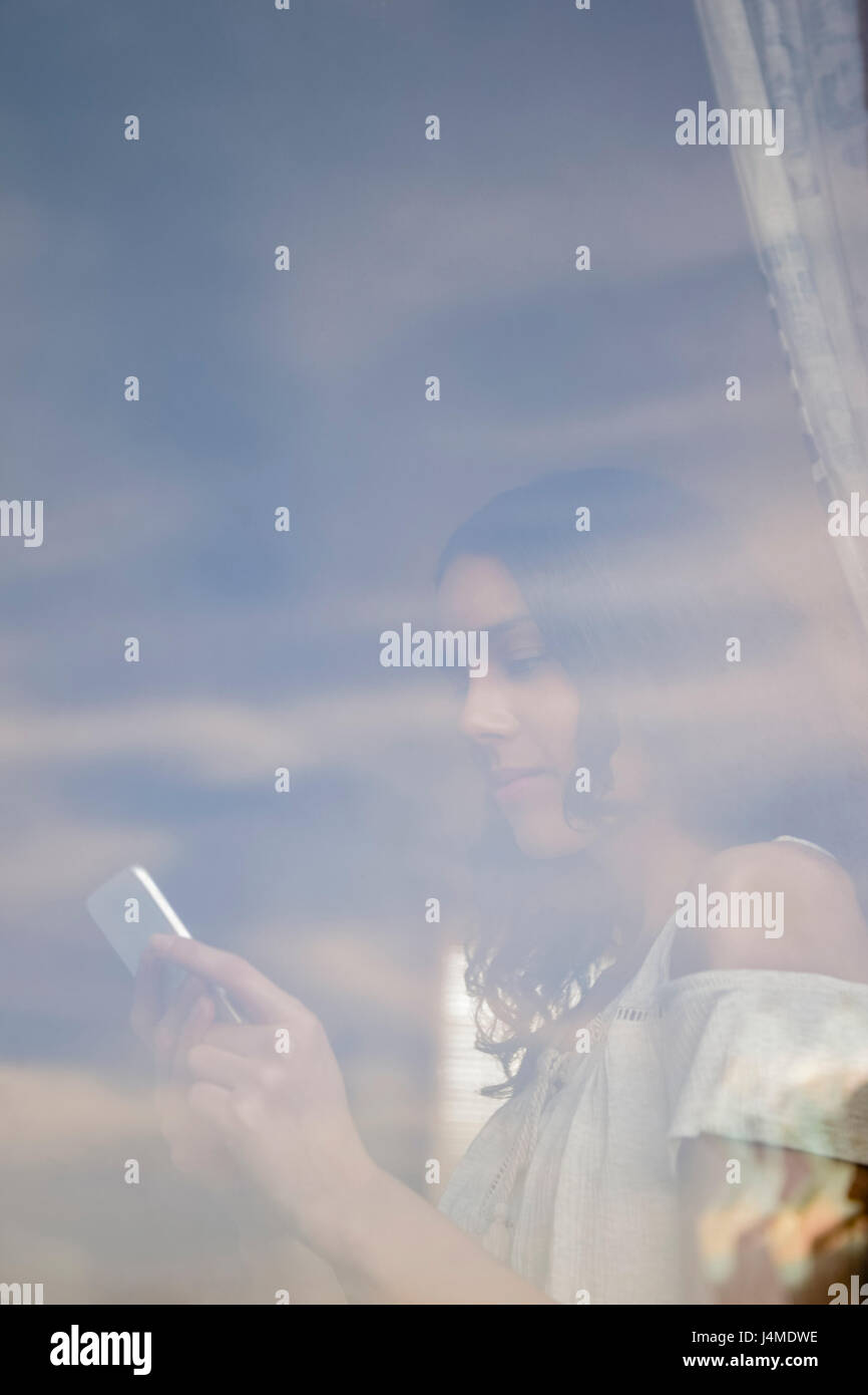Hispanic woman texting on cell phone behind window Stock Photo - Alamy