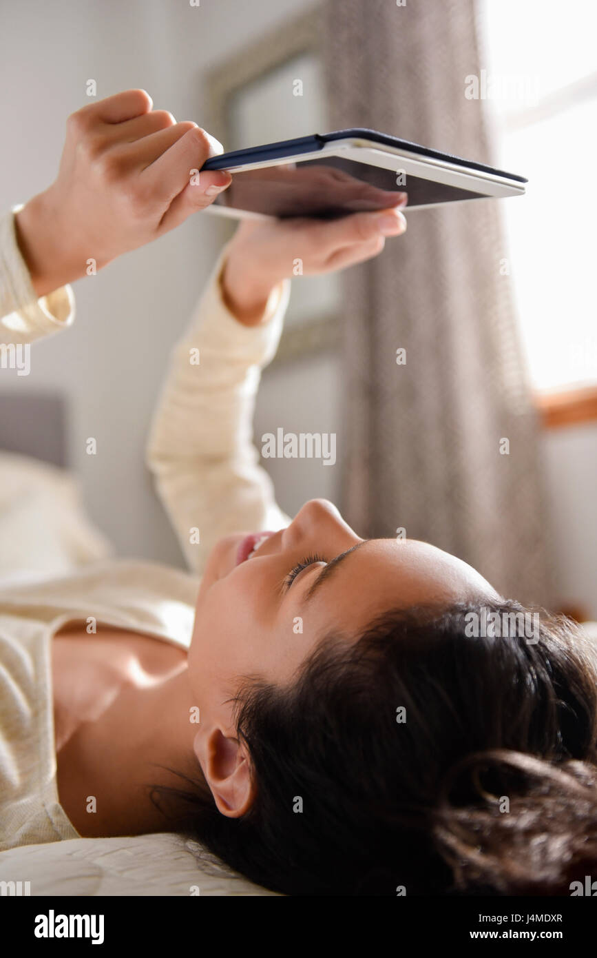 Hispanic woman laying on bed reading digital tablet Stock Photo
