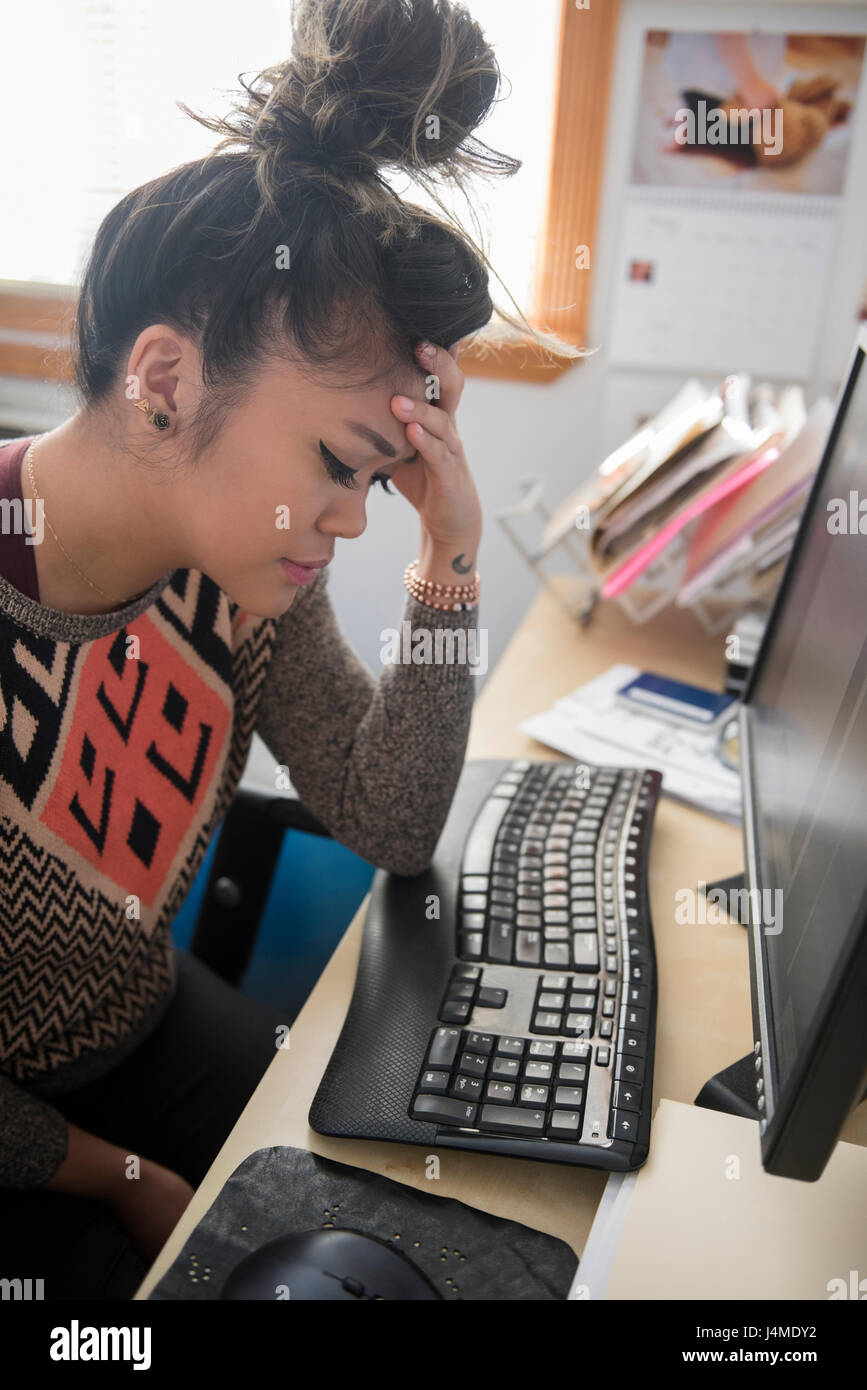 Frustrated Mixed Race woman sitting at desk using computer Stock Photo