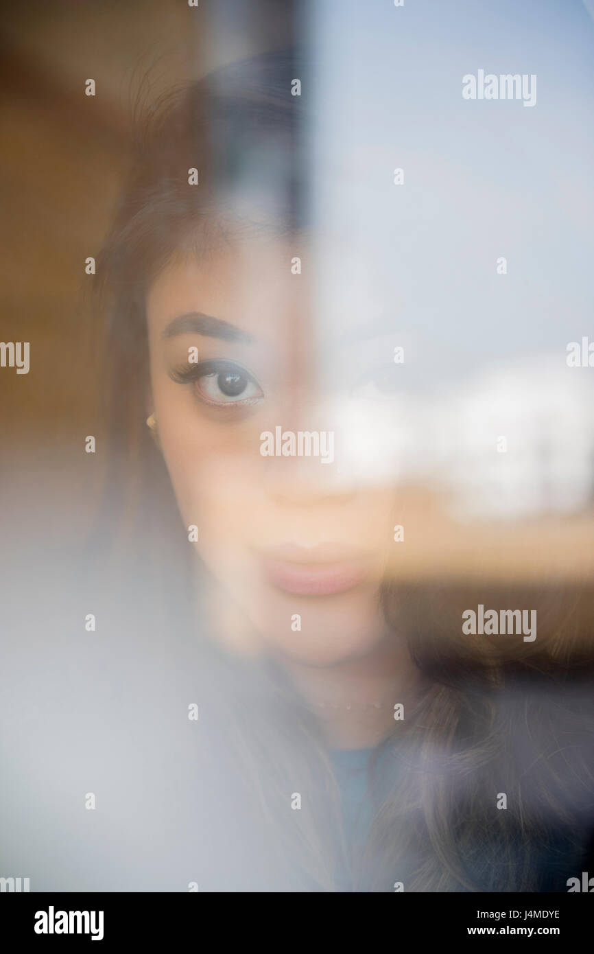 Face of serious Mixed Race woman behind window Stock Photo