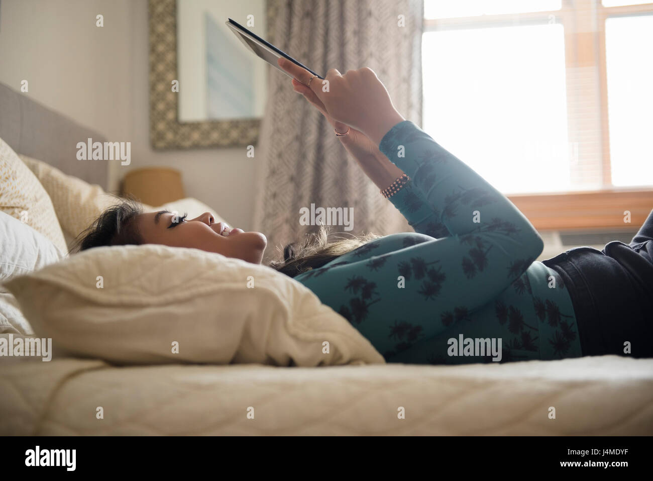 Mixed Race woman laying on bed using digital tablet Stock Photo