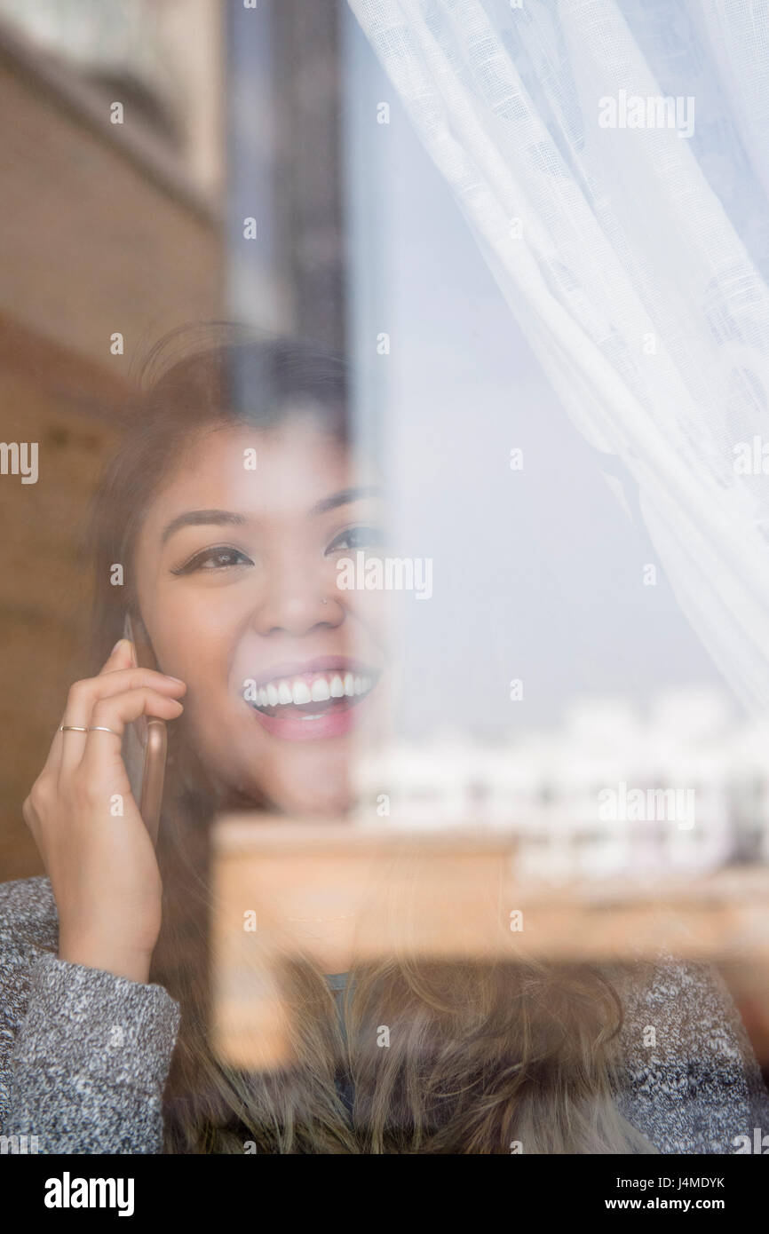 Mixed Race woman talking on cell phone behind window Stock Photo