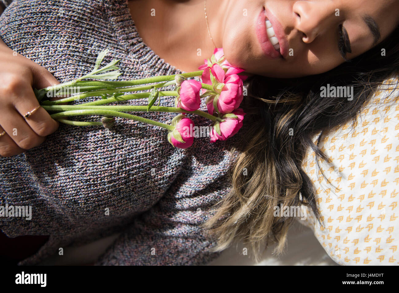 Mixed Race woman laying on bed holding flowers Stock Photo