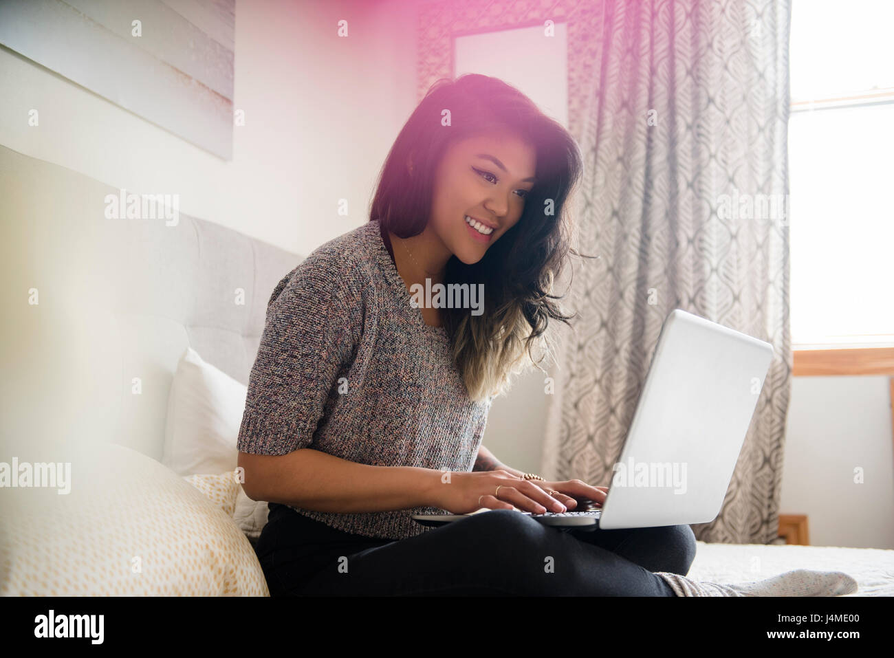 Mixed Race woman sitting on bed using laptop Stock Photo