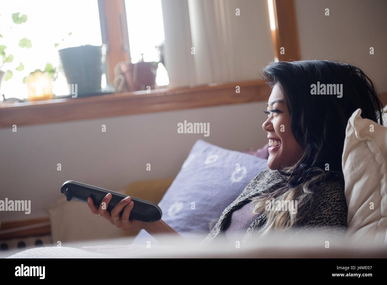 Smiling Mixed Race woman holding remote control and watching television Stock Photo