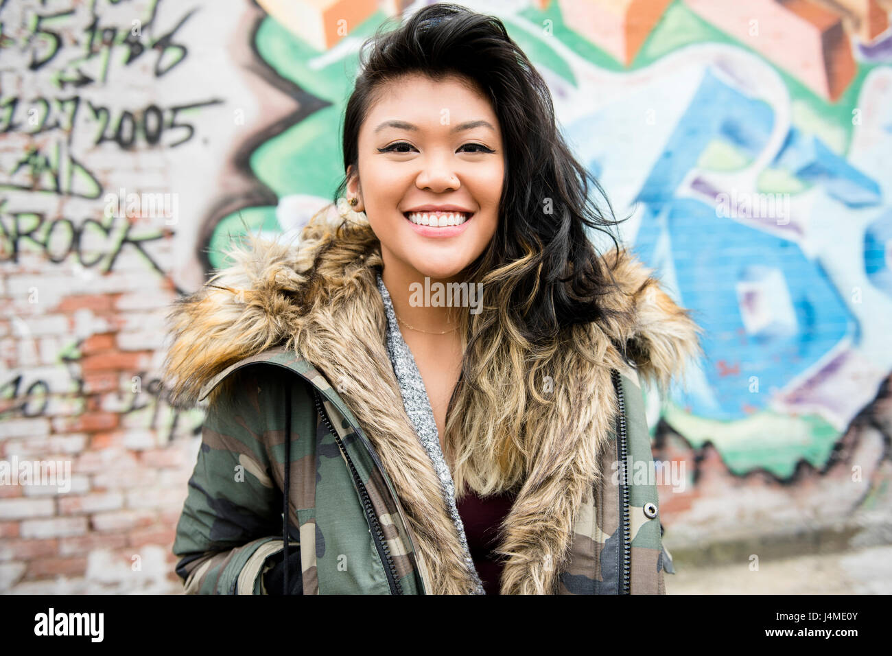 Portrait of smiling Mixed Race woman standing near graffiti Stock Photo