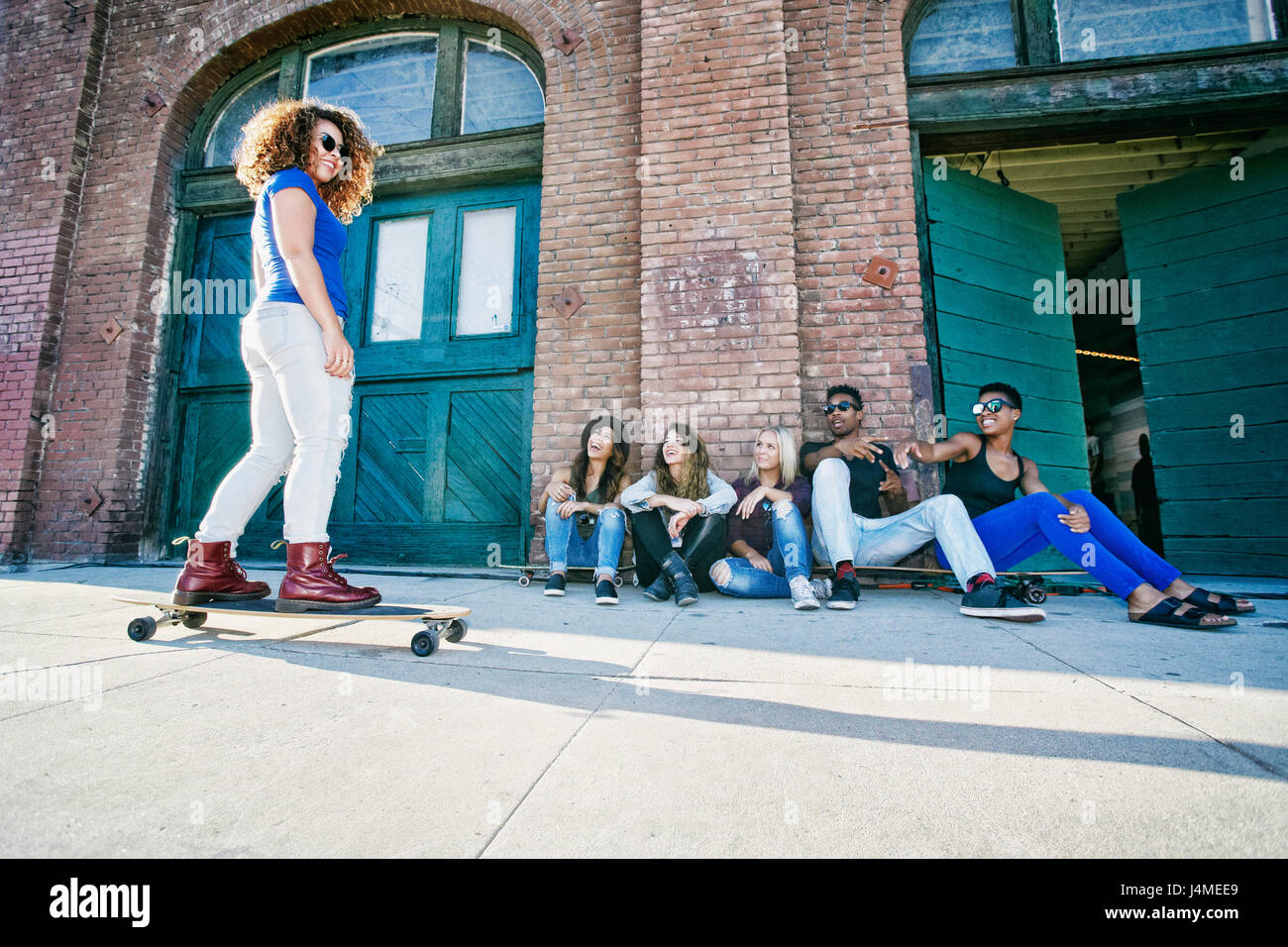 Friends watching woman skateboarding on sidewalk Stock Photo Alamy