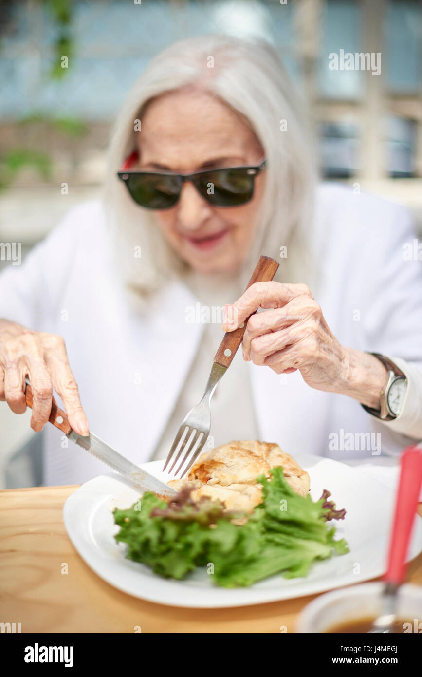 Older Caucasian woman cutting food on plate Stock Photo