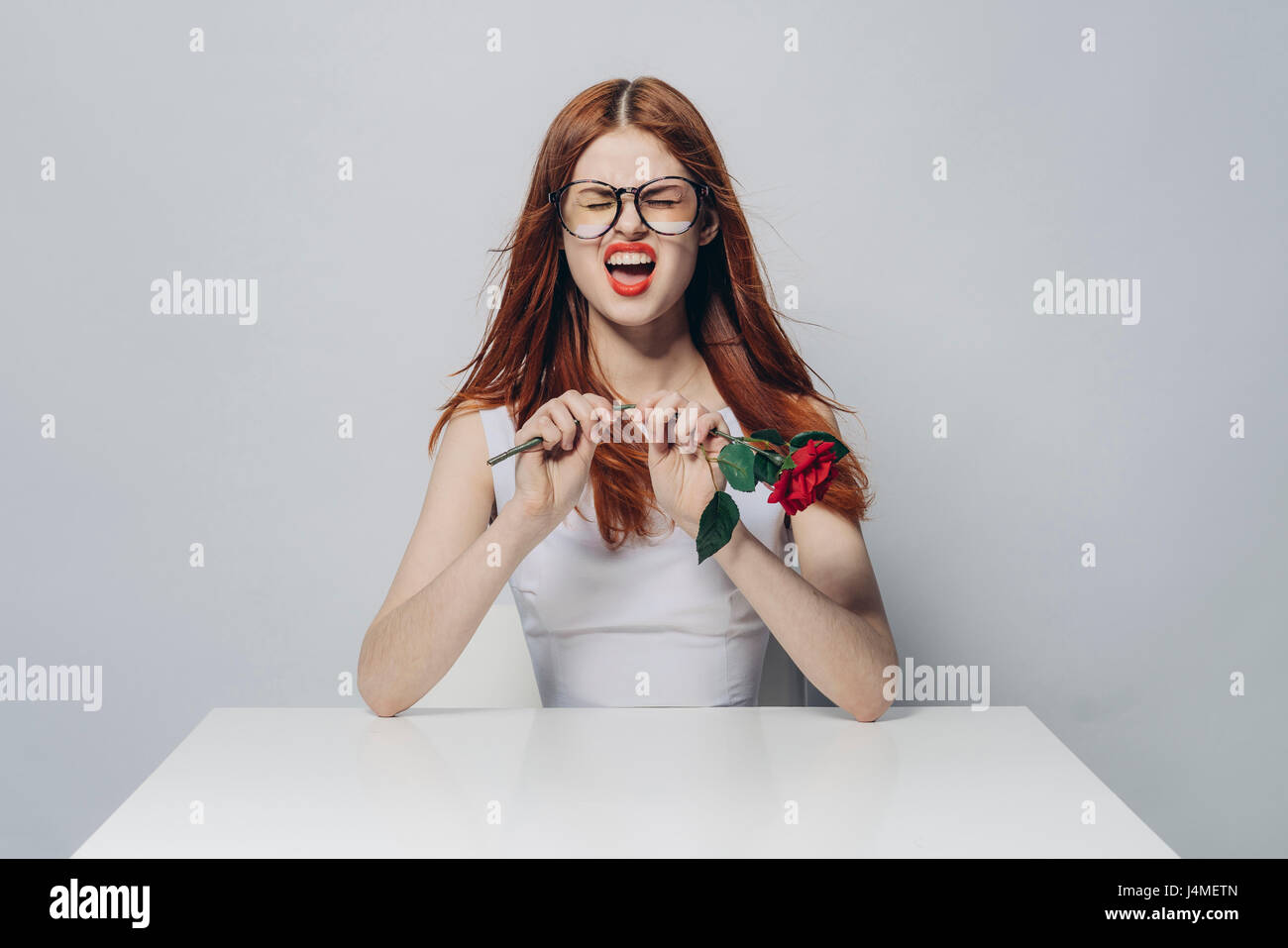 Caucasian woman sitting at windy table snapping stem of rose Stock ...