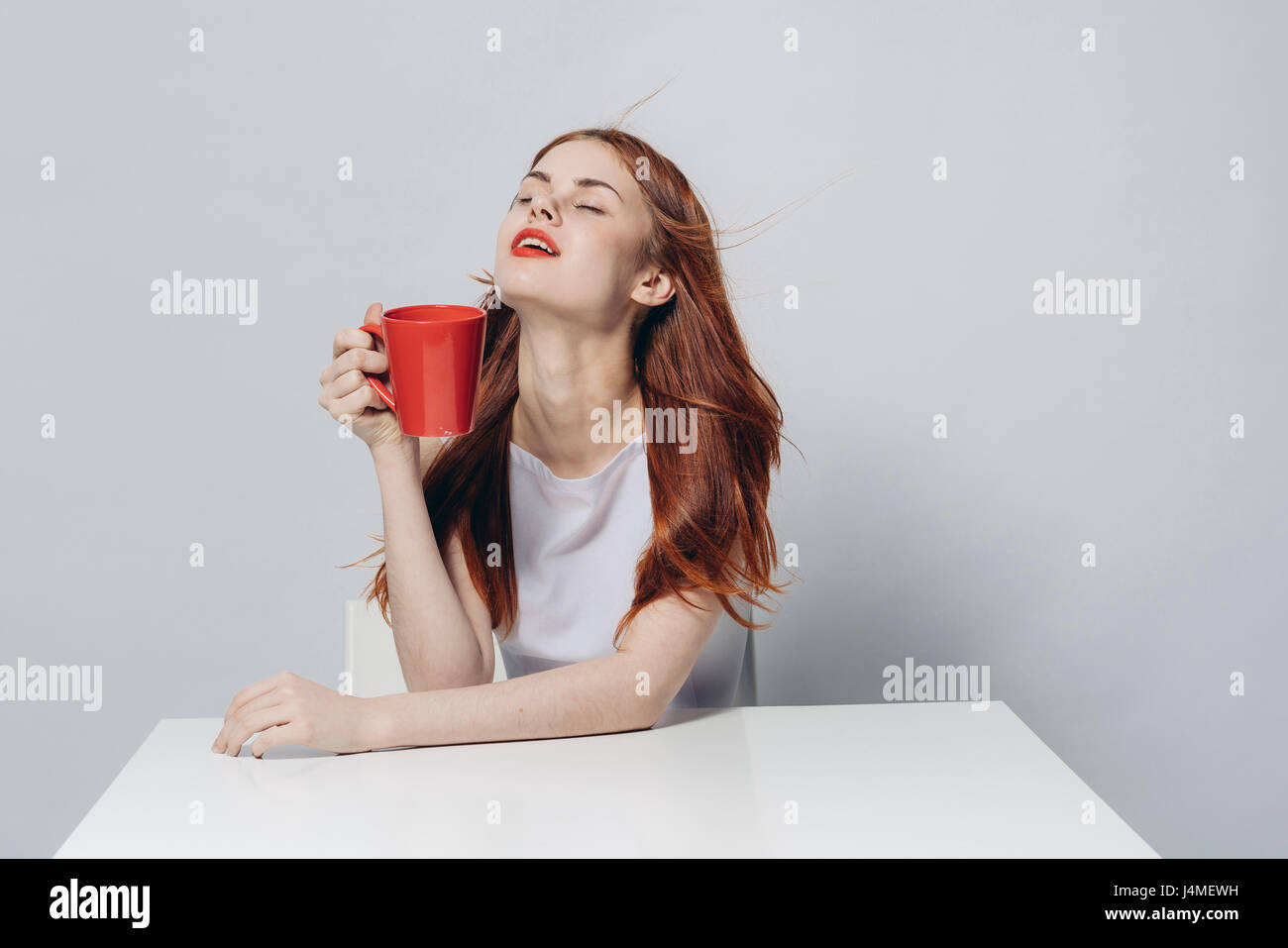 Caucasian woman sitting at windy table holding red cup Stock Photo