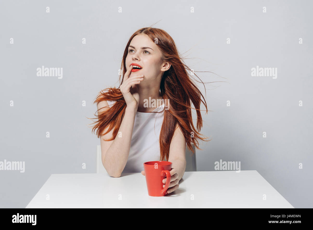 Pensive Caucasian woman sitting at windy table holding red cup Stock Photo