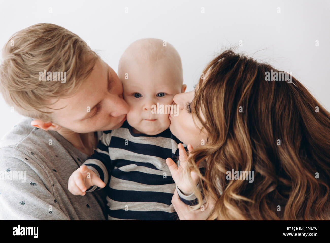 Caucasian mother and father kissing baby son on cheek Stock Photo