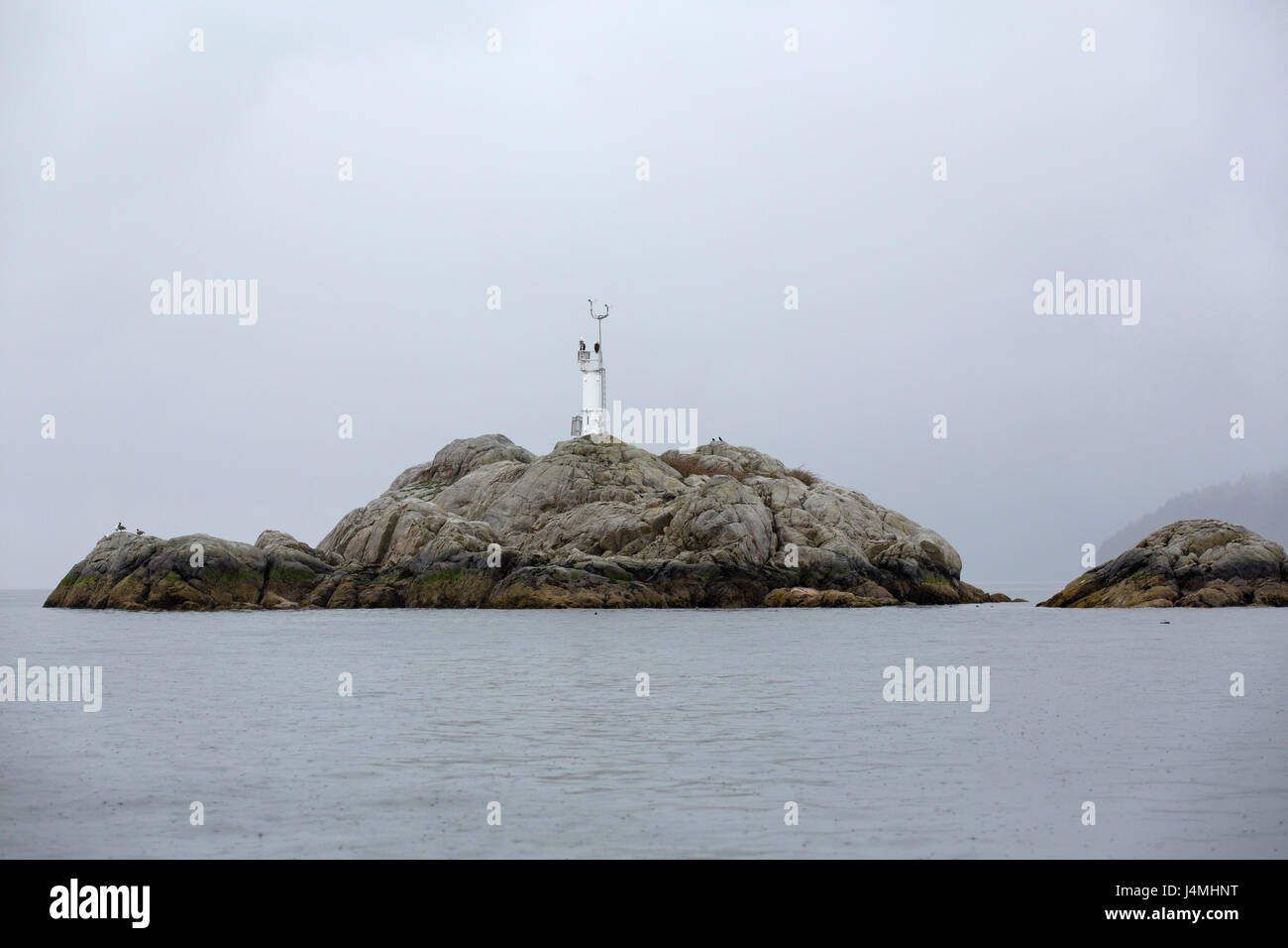 Weather station on a rocky island in the  Howe Sound near Vancouver, Canada. The birds rest on the pylon. Stock Photo