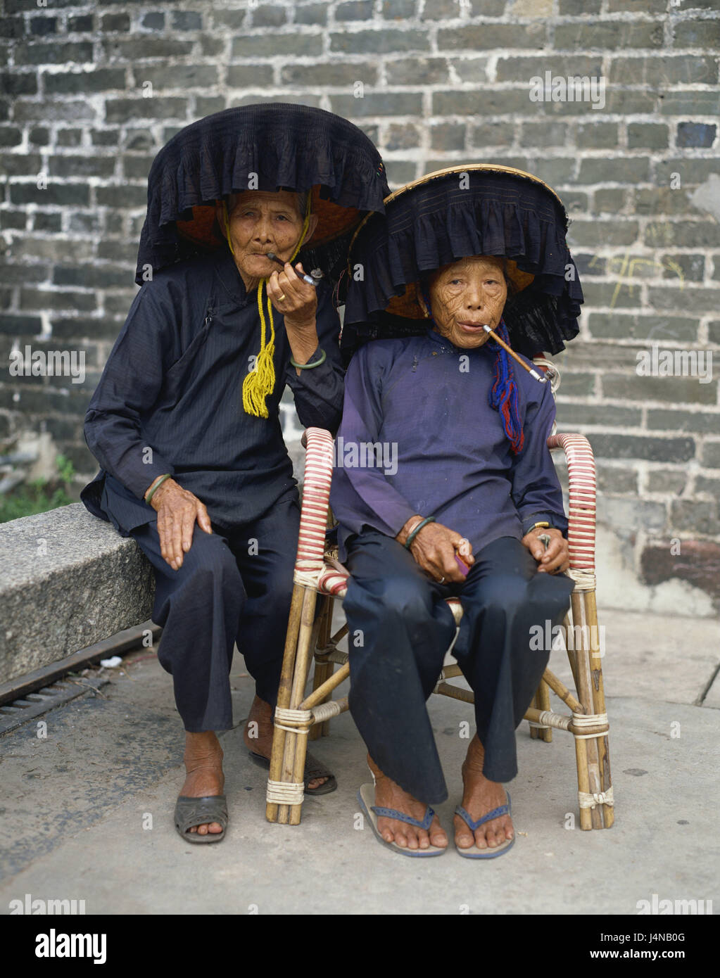 China, Hong Kong, Kowloon, New Territories, Coming Tin, Hakka women, Asia, town, city, cosmopolitan city, metropolis, mainland, peninsula, person, women, old, seniors, national costume, senior citizens, tribe, ethnic group Hakka, two, sit, smoke, whistle, care, headgear, traditionally, place of interest, outside, Stock Photo