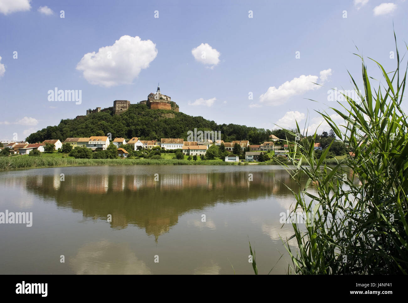 Austria, Burgenland, Stremtal, fishpond, reflexion, lock mountain, castle Güssing, town view, fishpond, castle, height castle, castle grounds, landmark, place of interest, tourism, houses, residential houses, sunshine, pond, sky, blue, clouds, reed, grass, Stock Photo