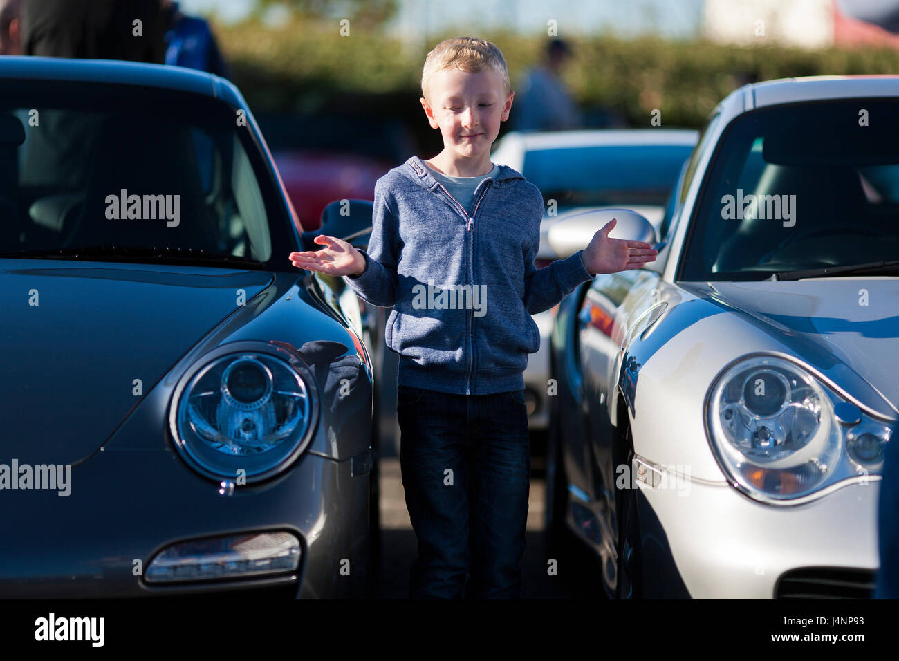 A small young boy stands between two Porsche super cars at a cars and coffee meeting in Liverpool, Merseyside Stock Photo