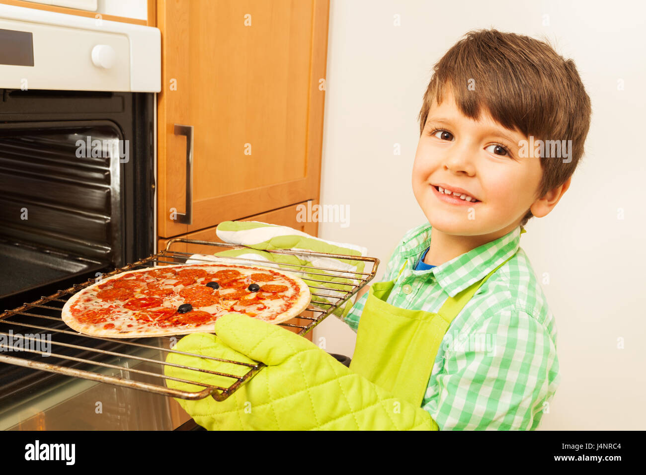 Closeup portrait of happy kid boy putting homemade pizza in the oven
