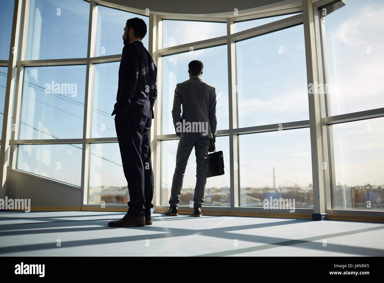 Two businessmen in suits standing inside office center Stock Photo - Alamy