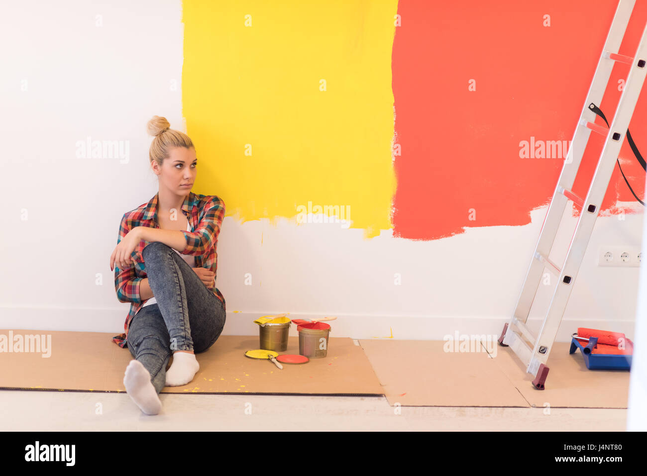 Portrait of a beautiful young female painter sitting on floor near wall ...