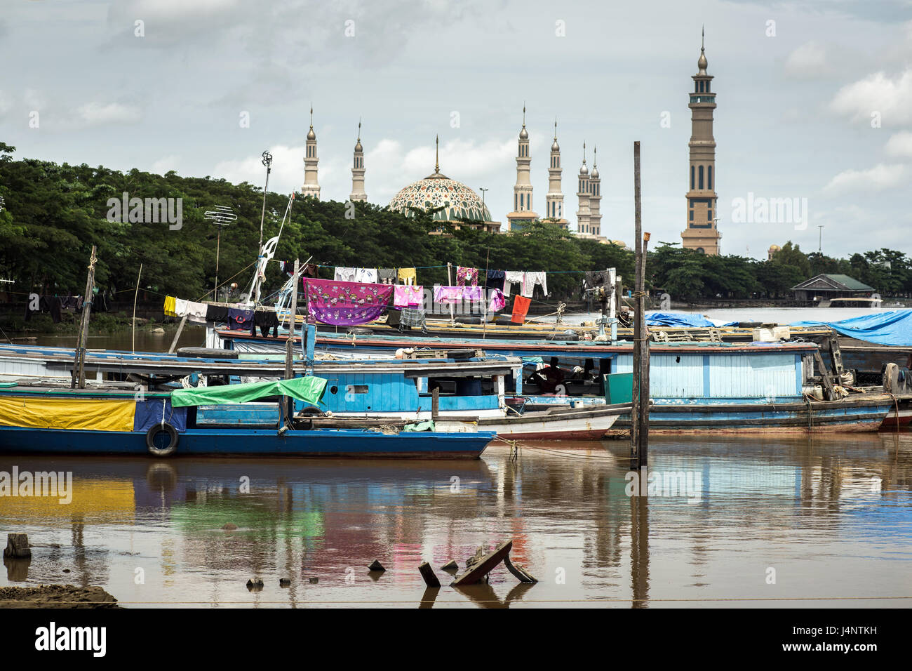 Colorful river boats and lifestyle on the Mahakam river of the peoples of Indonesian Borneo with Samarinda Islamic Center mosque in  the background Stock Photo