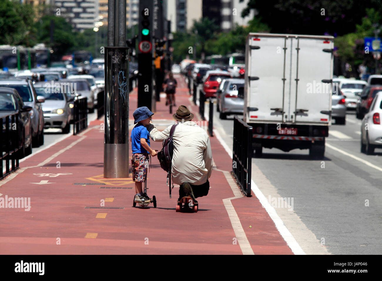 Father skateboarding and son riding a scooter on the cycle path of Paulista avenue - São Paulo city - Brazil Stock Photo