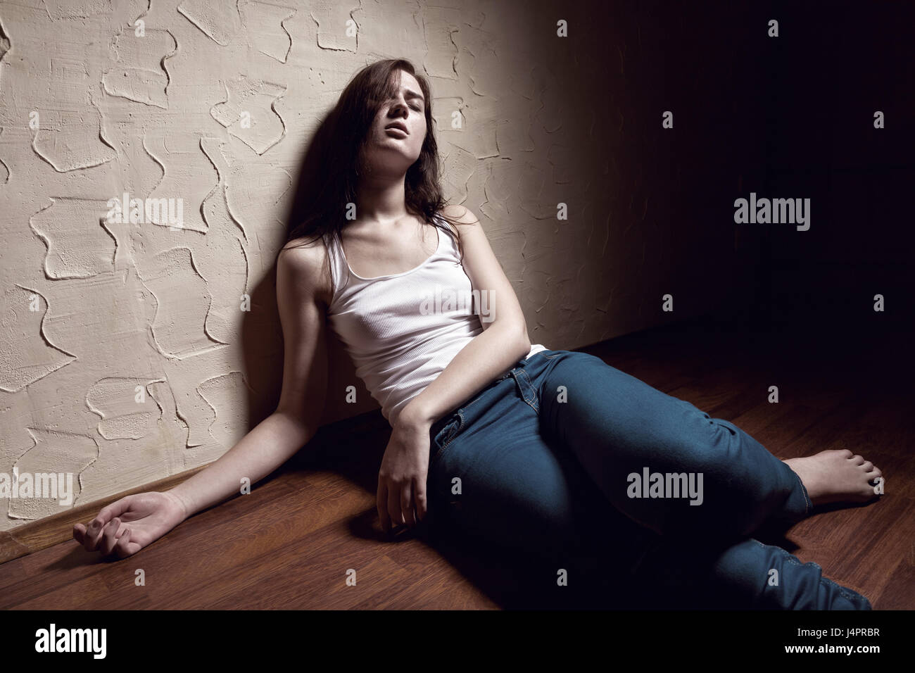 Girl addict unconscious sitting on the floor Stock Photo