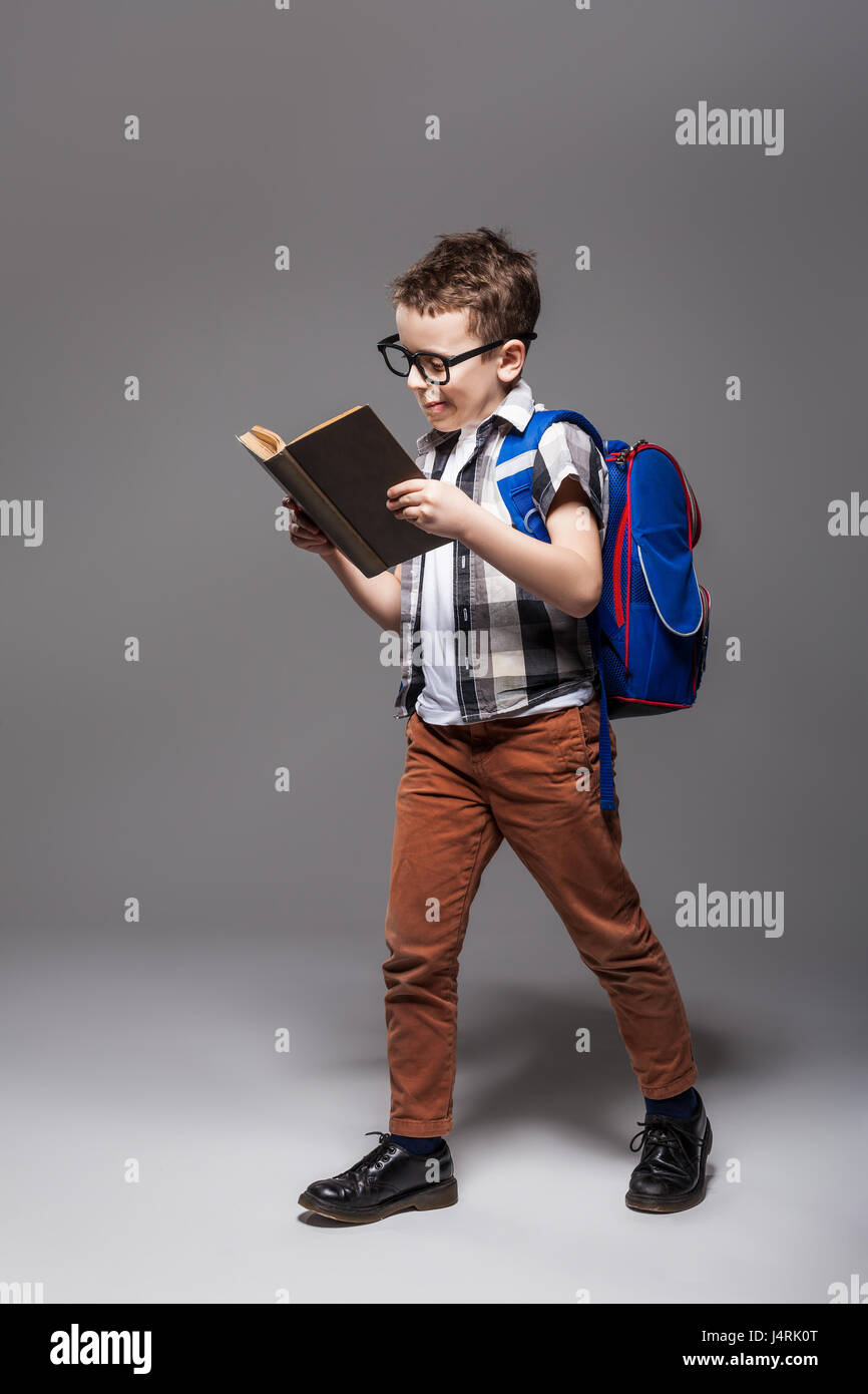 Little child with school bag reading a book, studio photo shoot. Young