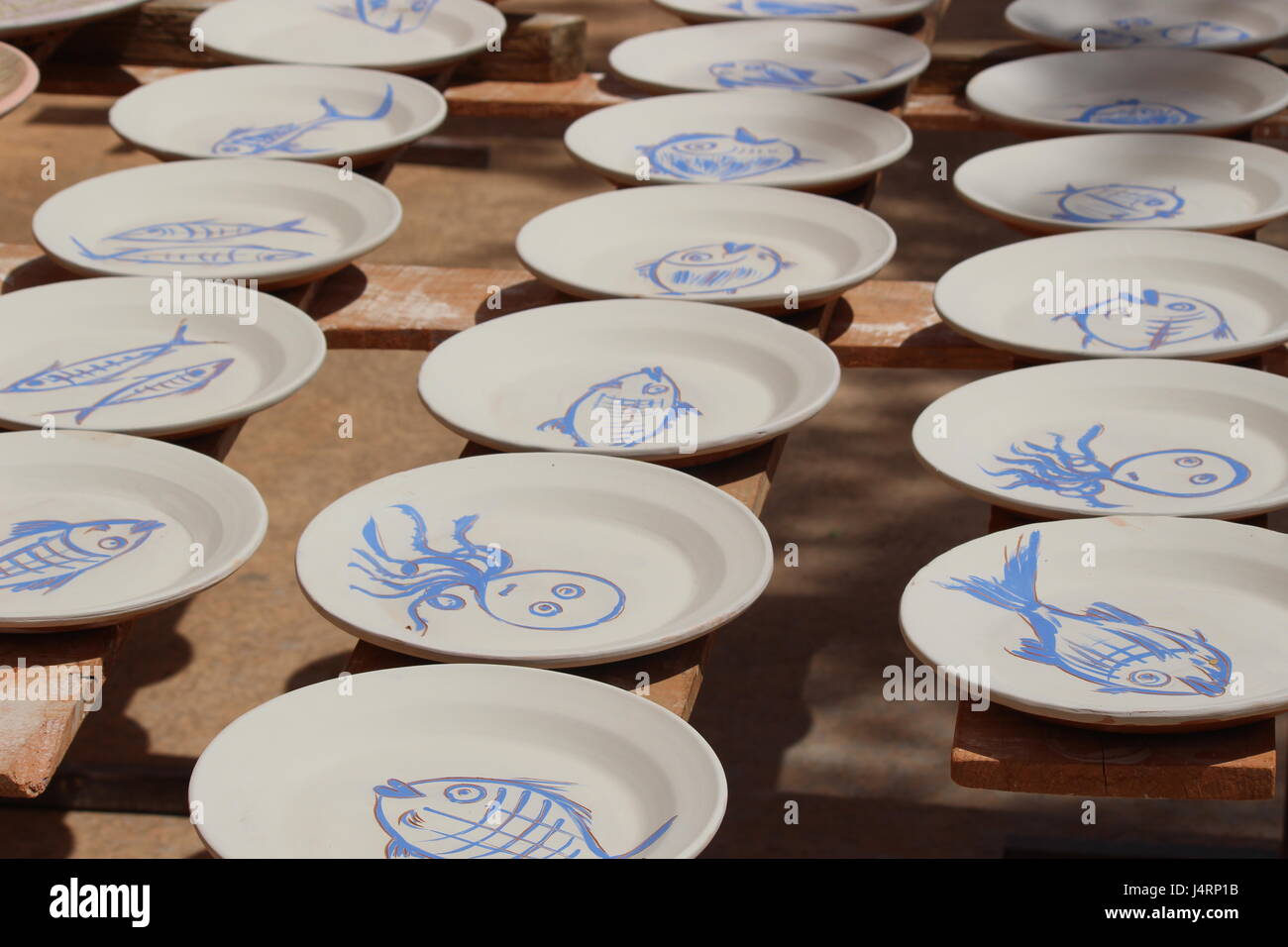 Spanish pottery plates with blue fish designs on white background drying on racks in sun Stock Photo