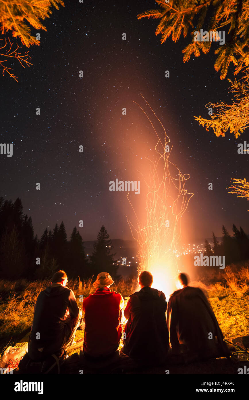 Four friends sitting near campfire in high mountains. Amazing night scene. Man friendship concept Stock Photo
