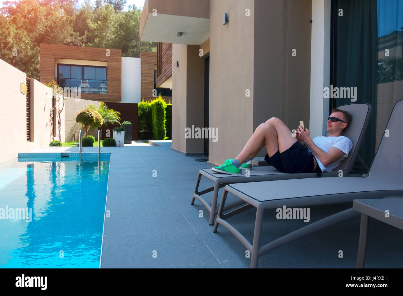 Man relaxing on lounge near modern houses with swimming pool. Actual eco architecture Stock Photo