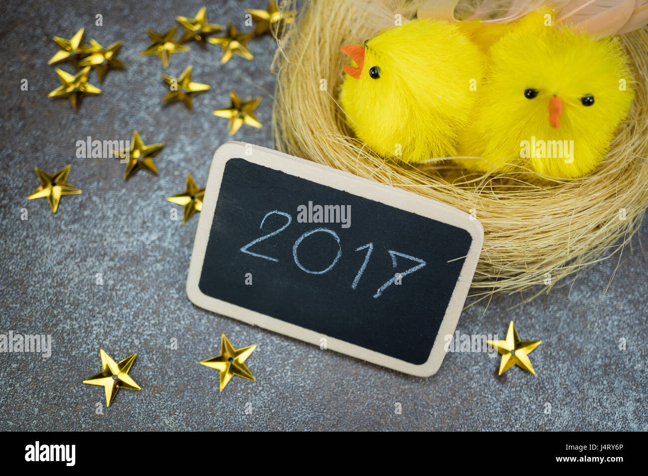 Little chicks in the nest  with  greeting  blackboard and golden stars on rustic tile background Stock Photo