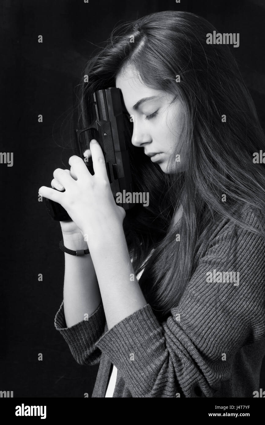 Monochrome close up emotional portrait of young beautiful girl with a gun Stock Photo