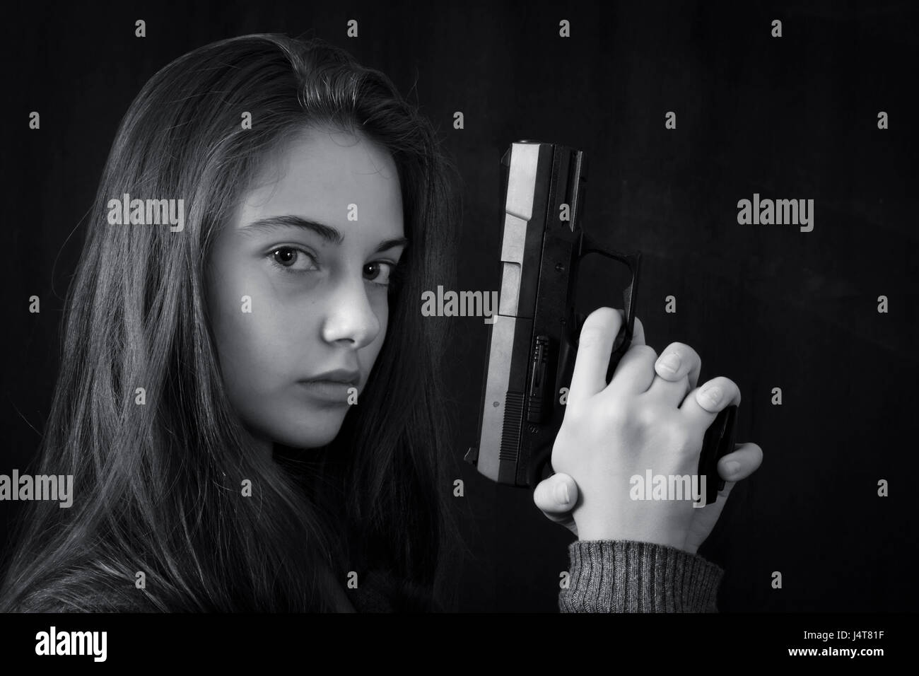 Monochrome close up emotional portrait of young beautiful girl with a gun Stock Photo