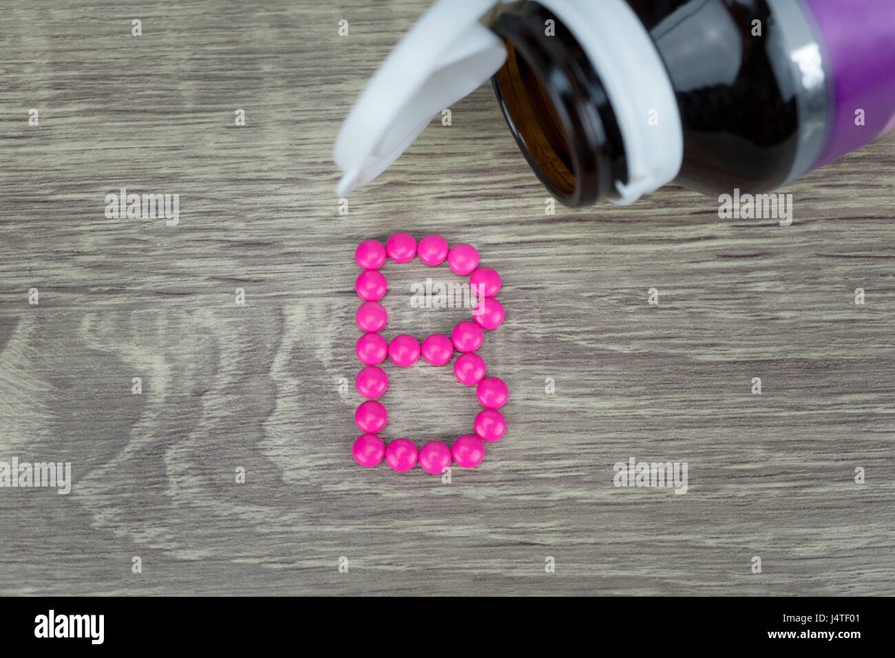 Pink pills forming shape to B alphabet on wood background Stock Photo