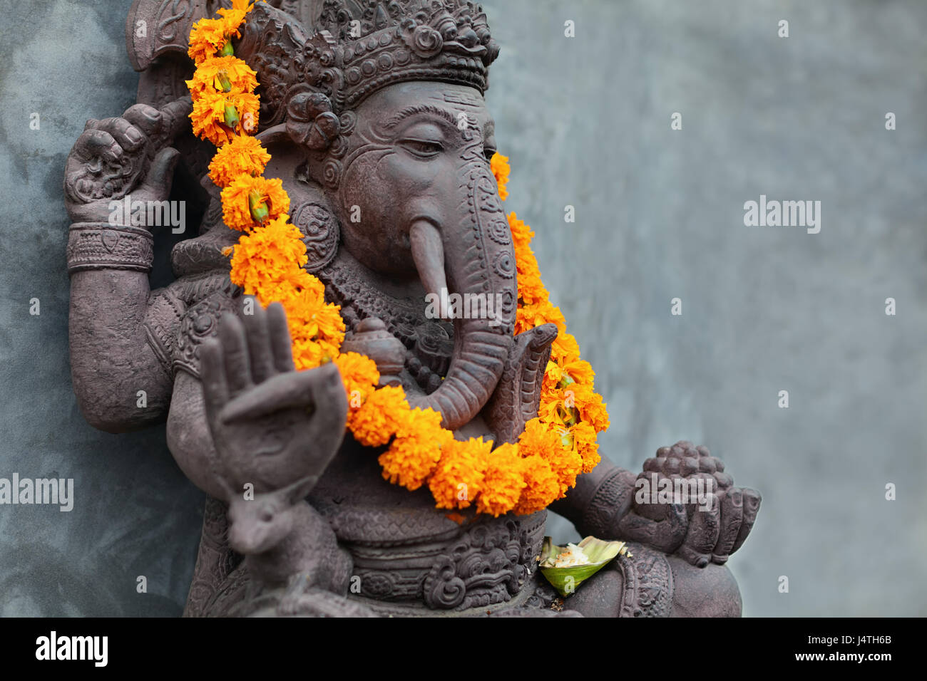 Ganesha with balinese Barong masks sitting on front of temple. Decorated for religious festival by orange flowers necklace and ceremonial offering. Tr Stock Photo